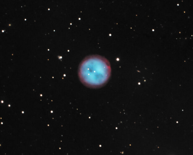 Der planetarische Eulennebel M97 als runde, blassgrüne Scheibe mit zwei dunkleren Flecken, die wie Augen wirken