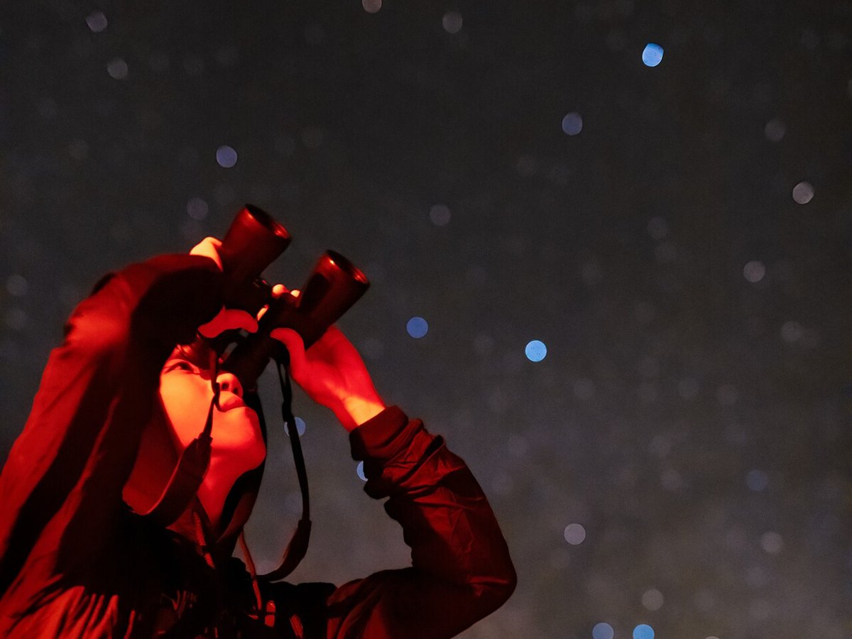 Persona observando la Vía Láctea con prismáticos bajo luz roja