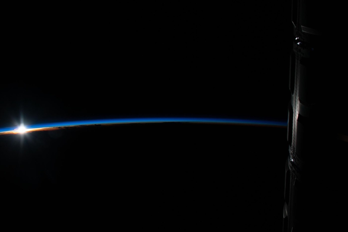 Sonnenaufgang über dem Erdrand mit leuchtender blauer Atmosphäre, aufgenommen von der ISS