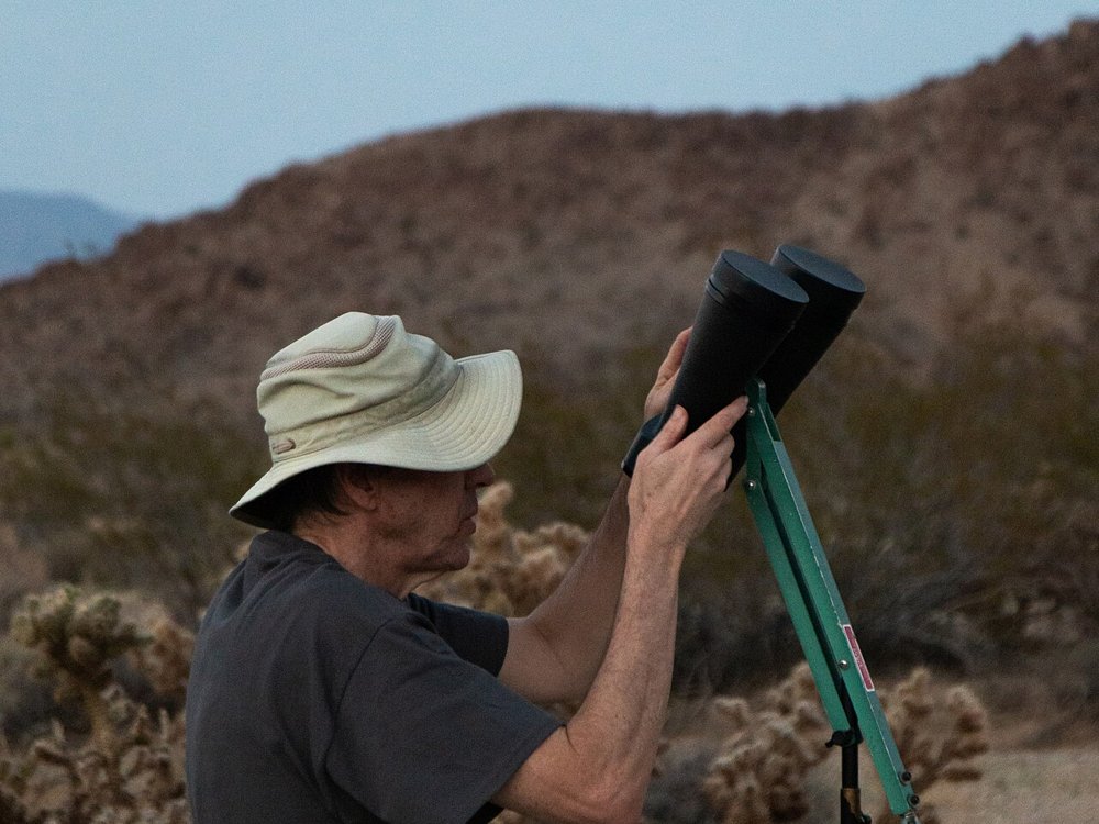 Un osservatore punta un grande binocolo astronomico su un supporto a parallelogramma montato su treppiede
