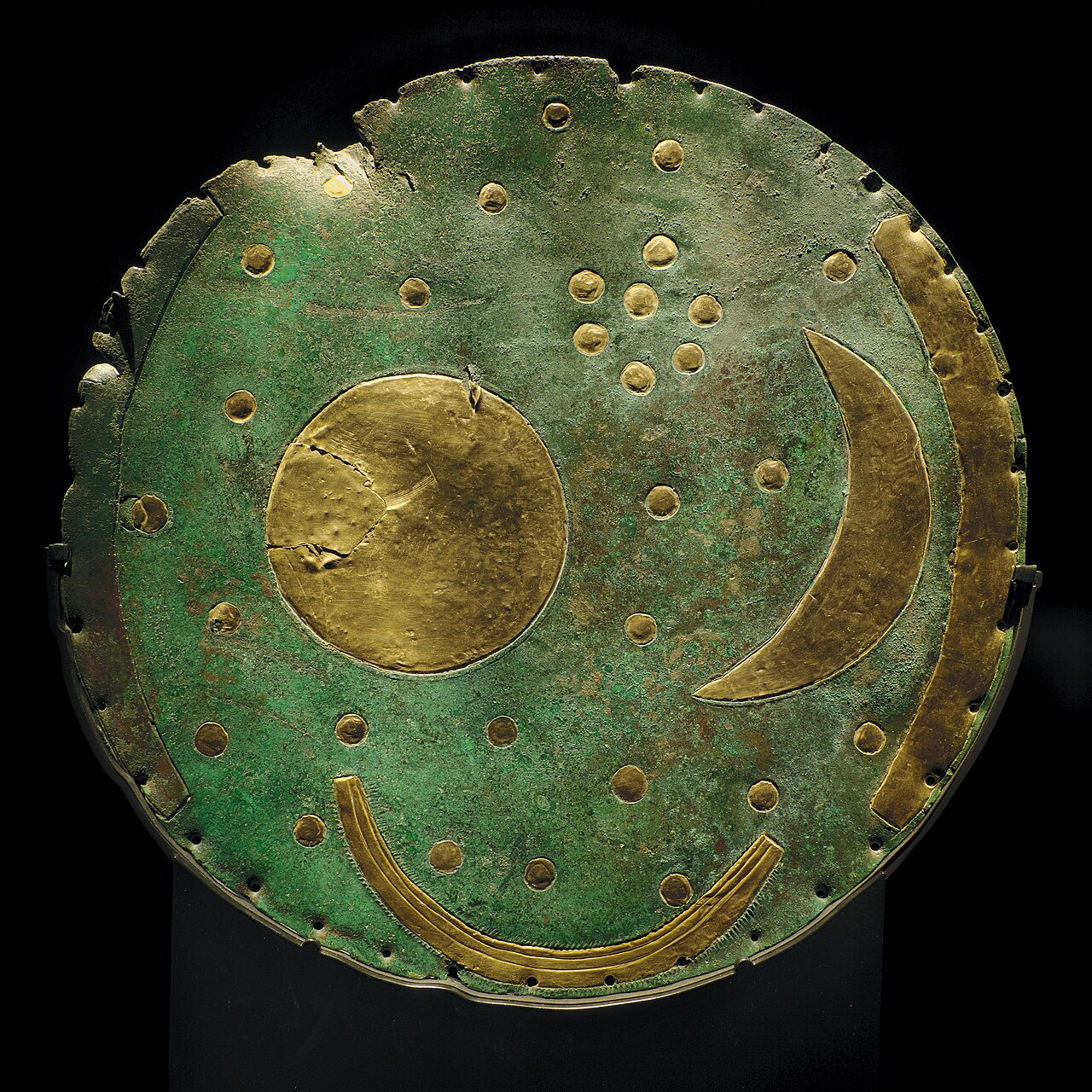 Die Himmelsscheibe von Nebra: grüne Bronzescheibe mit goldenem Vollmond, Mondsichel, Sternen, Randbogen und Barke