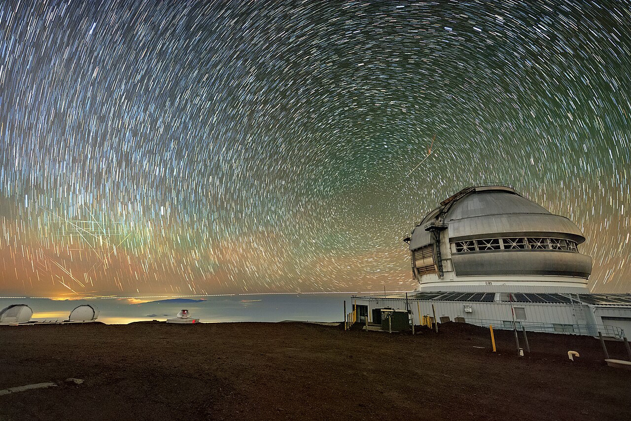 Sternenhimmel über der Kuppel des Gemini-North-Teleskops, links ziehen mehrere Satelliten als unterbrochene Lichtstreifen durchs Bild