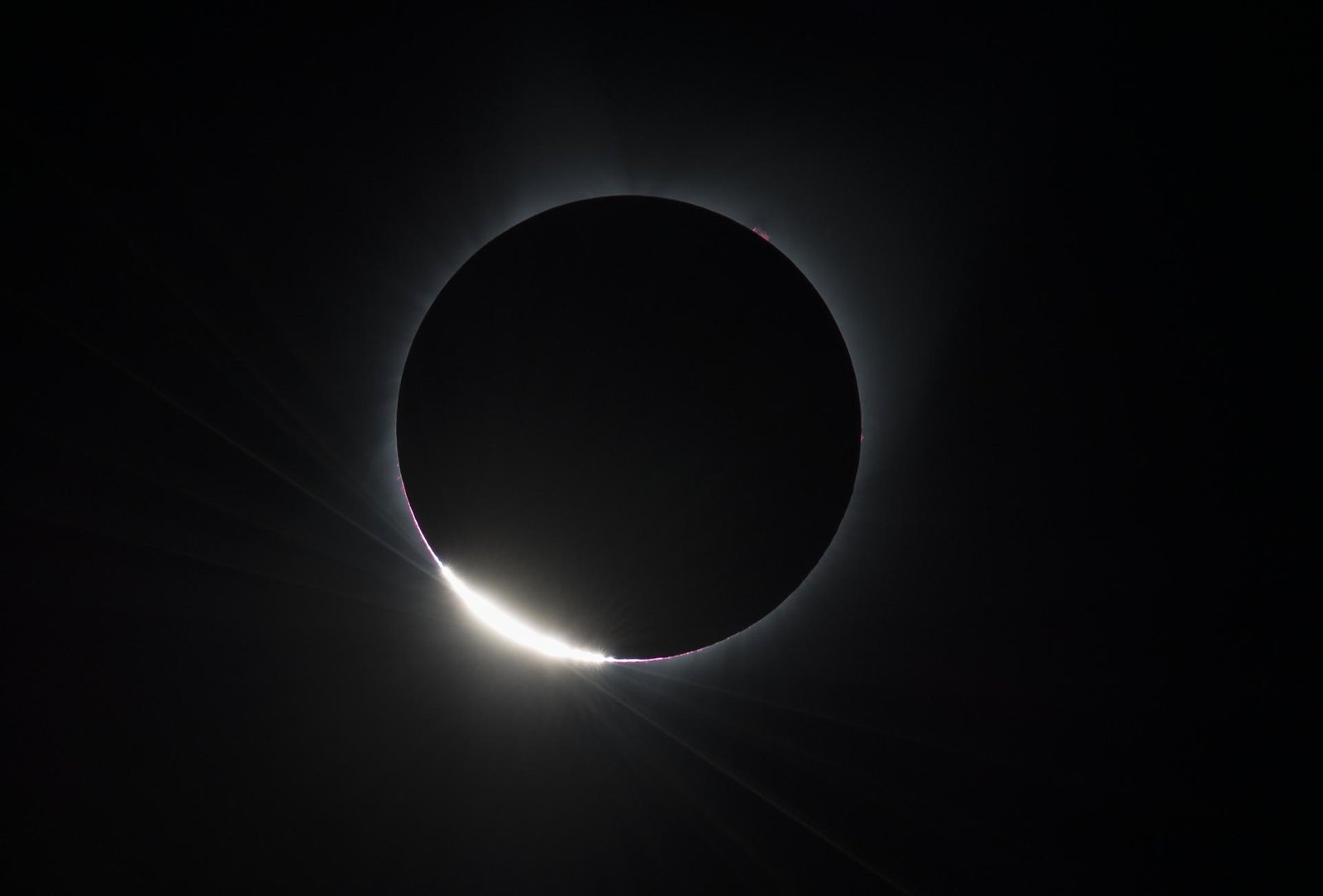 Diamantring bei einer totalen Sonnenfinsternis: heller Lichtpunkt am Rand der schwarzen Mondscheibe, umgeben von der Korona
