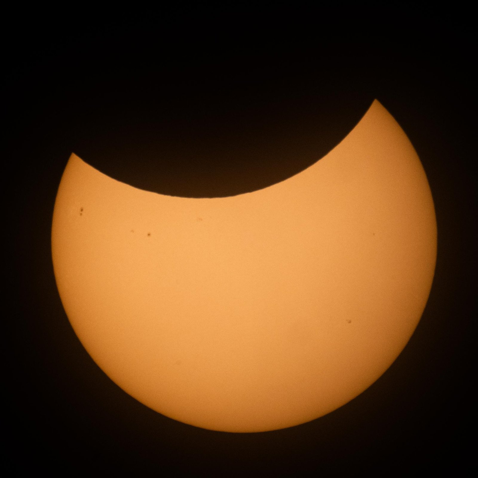 Partiell vom Mond bedeckte Sonne als orange Scheibe mit Sichelform, fotografiert durch einen Sonnenfilter