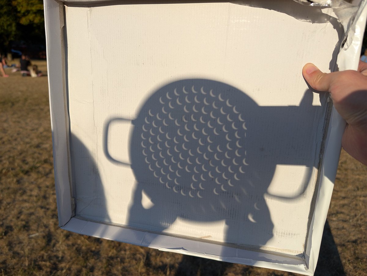 Schatten eines Nudelsiebs auf weißem Karton während der Sonnenfinsternis: jedes Loch projiziert eine kleine Sonnensichel